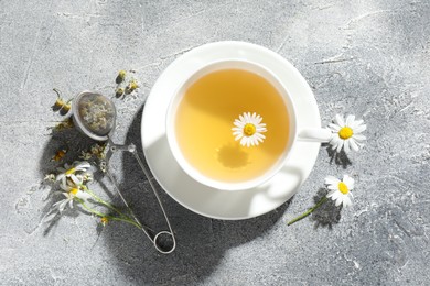 Photo of Tasty chamomile tea, infuser and flowers on light grey table, flat lay