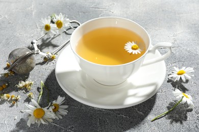 Photo of Tasty chamomile tea, infuser and flowers on light grey table, closeup