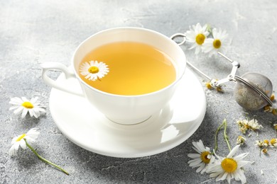 Photo of Tasty chamomile tea, infuser and flowers on light grey table, closeup