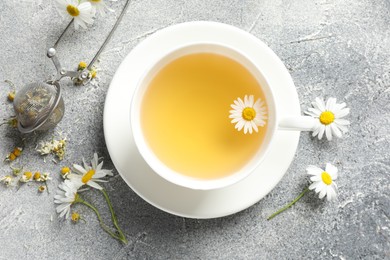 Photo of Tasty chamomile tea, infuser and flowers on light grey table, flat lay