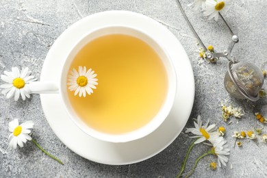 Photo of Tasty chamomile tea, infuser and flowers on light grey table, flat lay