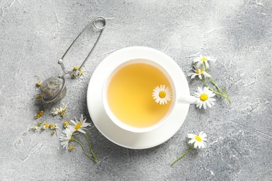 Photo of Tasty chamomile tea, infuser and flowers on light grey table, flat lay