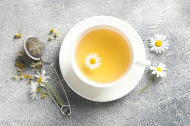 Photo of Tasty chamomile tea, infuser and flowers on light grey table, flat lay