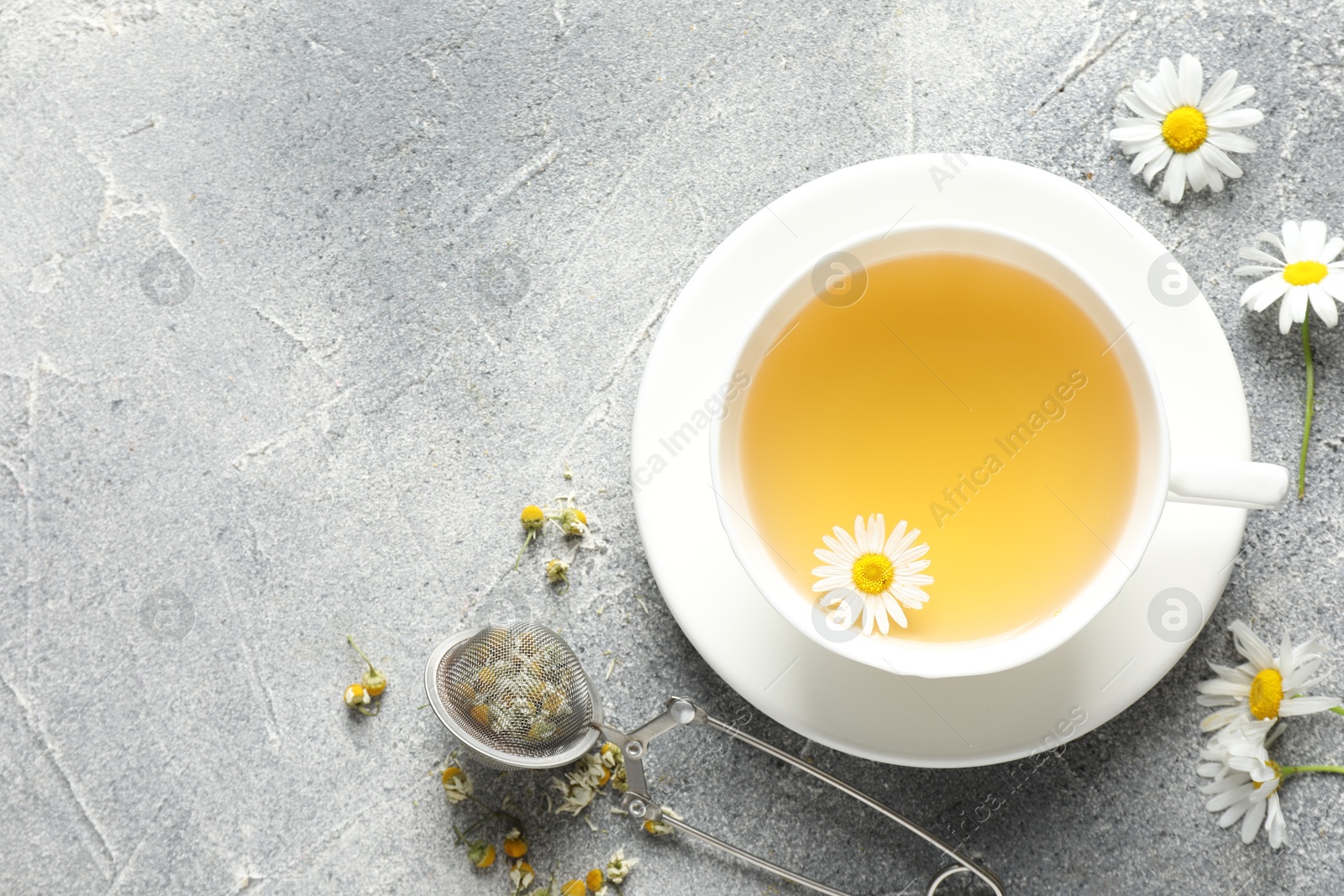 Tasty chamomile tea, infuser and flowers on light grey table, flat lay. Space for text Photo of Tasty chamomile tea, infuser and flowers on light grey table, flat lay. Space for text