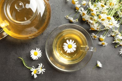 Photo of Tasty chamomile tea and flowers on grey table, flat lay