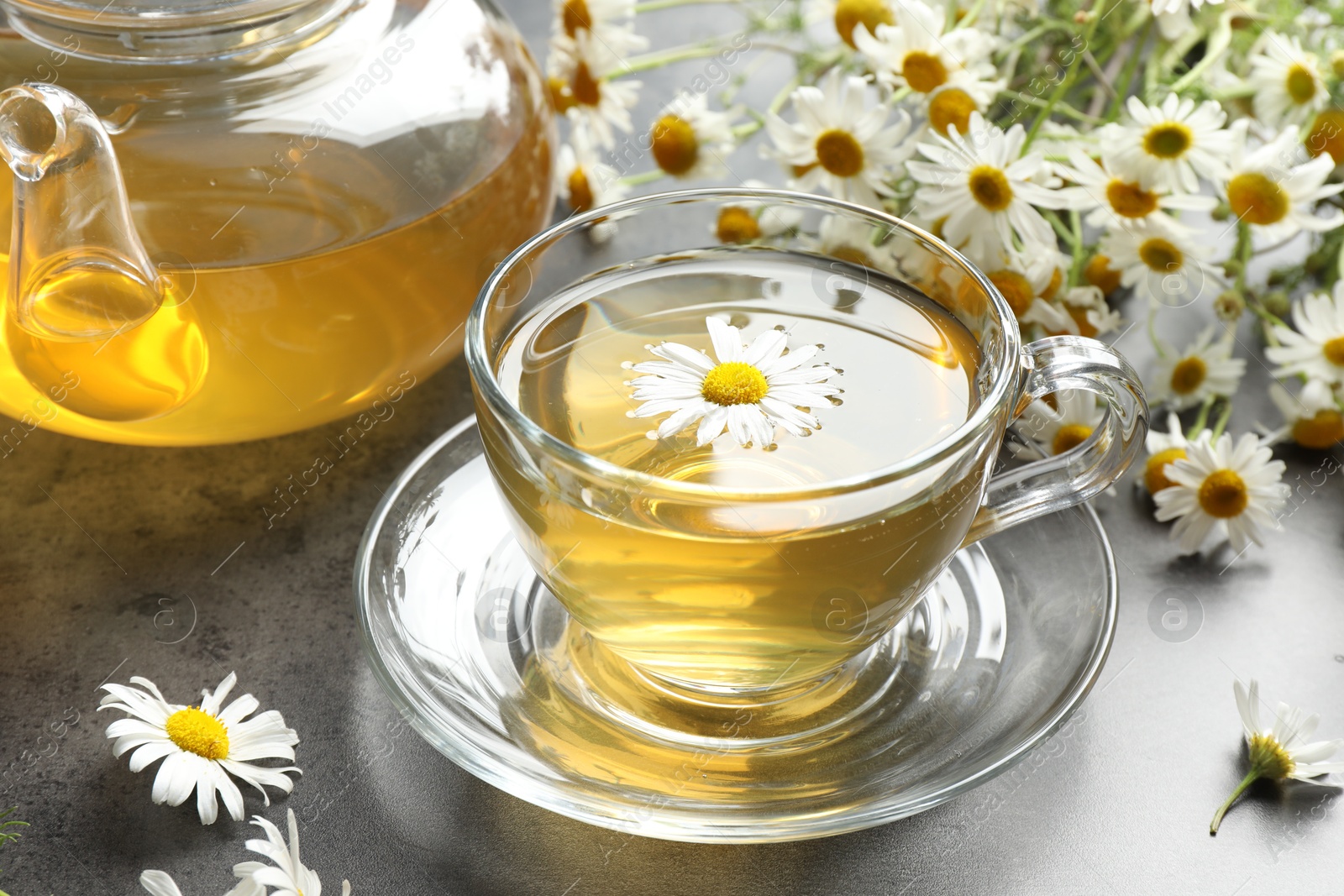 Tasty chamomile tea and flowers on grey table, closeup Photo of Tasty chamomile tea and flowers on grey table, closeup