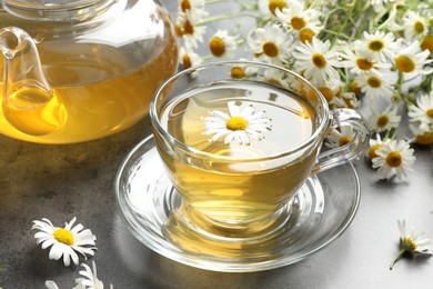 Photo of Tasty chamomile tea and flowers on grey table, closeup
