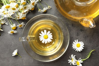 Photo of Tasty chamomile tea and flowers on grey table, flat lay