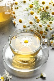 Photo of Tasty chamomile tea and flowers on grey table, closeup