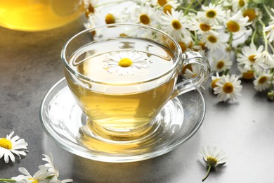 Photo of Tasty chamomile tea and flowers on grey table, closeup