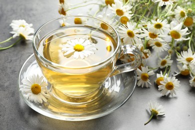Photo of Tasty chamomile tea and flowers on grey table, closeup