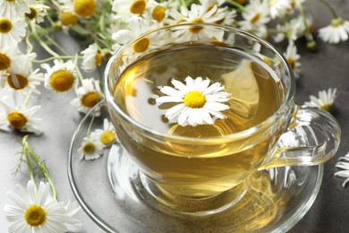 Photo of Tasty chamomile tea and flowers on grey table, closeup