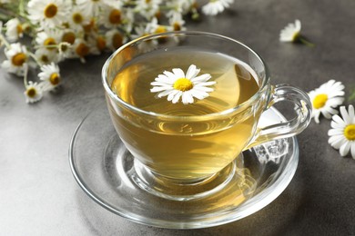 Photo of Tasty chamomile tea and flowers on grey table, closeup