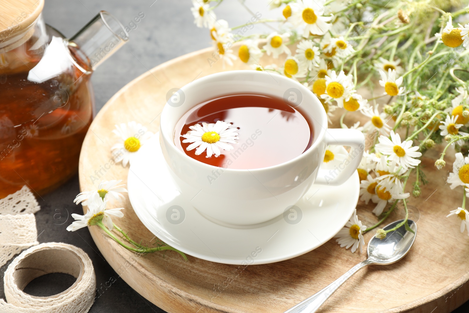 Photo of Tasty chamomile tea and flowers on black table, closeup