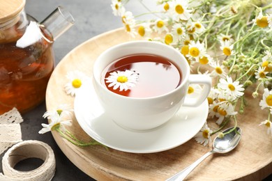 Photo of Tasty chamomile tea and flowers on black table, closeup