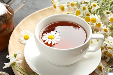 Photo of Tasty chamomile tea and flowers on black table, closeup