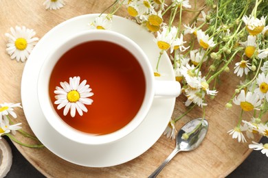 Photo of Tasty chamomile tea and flowers on black table, flat lay