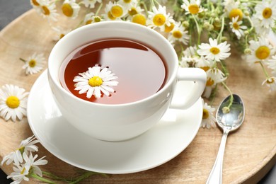 Photo of Tasty chamomile tea and flowers on black table, closeup