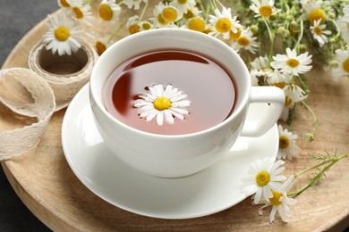 Photo of Tasty chamomile tea and flowers on black table, closeup