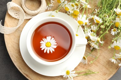 Photo of Tasty chamomile tea and flowers on black table, flat lay