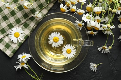 Photo of Tasty chamomile tea and flowers on black table, flat lay