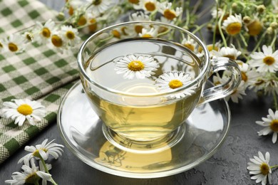 Photo of Tasty chamomile tea and flowers on black table, closeup