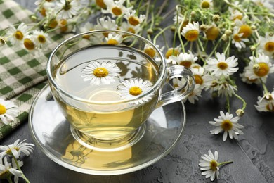 Photo of Tasty chamomile tea and flowers on black table, closeup