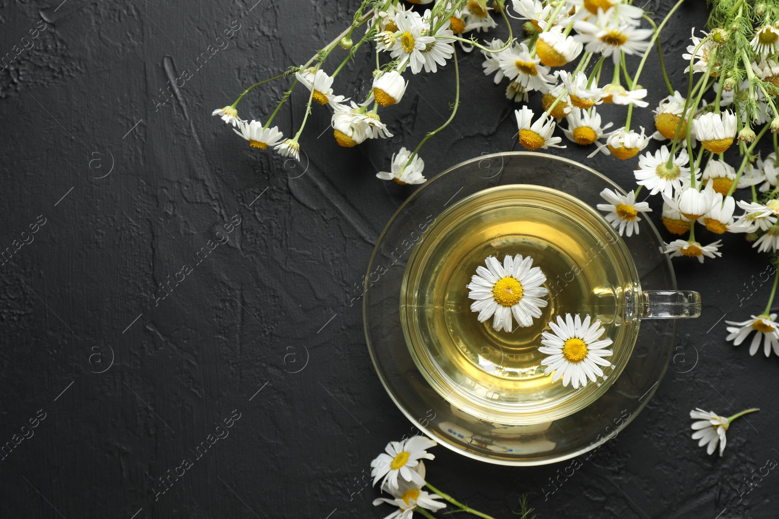 Tasty chamomile tea and flowers on black table, flat lay. Space for text Photo of Tasty chamomile tea and flowers on black table, flat lay. Space for text