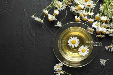 Photo of Tasty chamomile tea and flowers on black table, flat lay. Space for text
