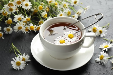 Photo of Tasty chamomile tea, infuser and flowers on black table, closeup