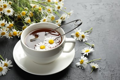 Photo of Tasty chamomile tea, infuser and flowers on black table, closeup. Space for text
