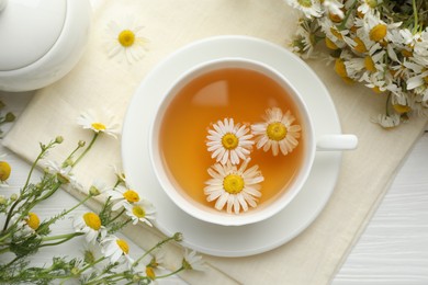Photo of Tasty chamomile tea and flowers on white wooden table, flat lay