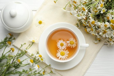 Photo of Tasty chamomile tea and flowers on white wooden table, flat lay