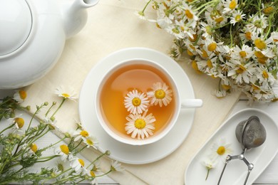 Photo of Tasty chamomile tea, infuser and flowers on white wooden table, flat lay