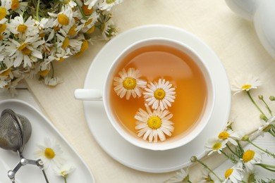 Photo of Tasty chamomile tea, infuser and flowers on white wooden table, flat lay