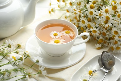 Photo of Tasty chamomile tea, infuser and flowers on white wooden table, closeup