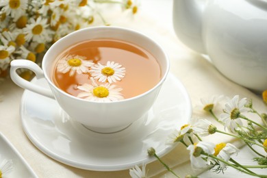 Photo of Tasty chamomile tea and flowers on white wooden table, closeup