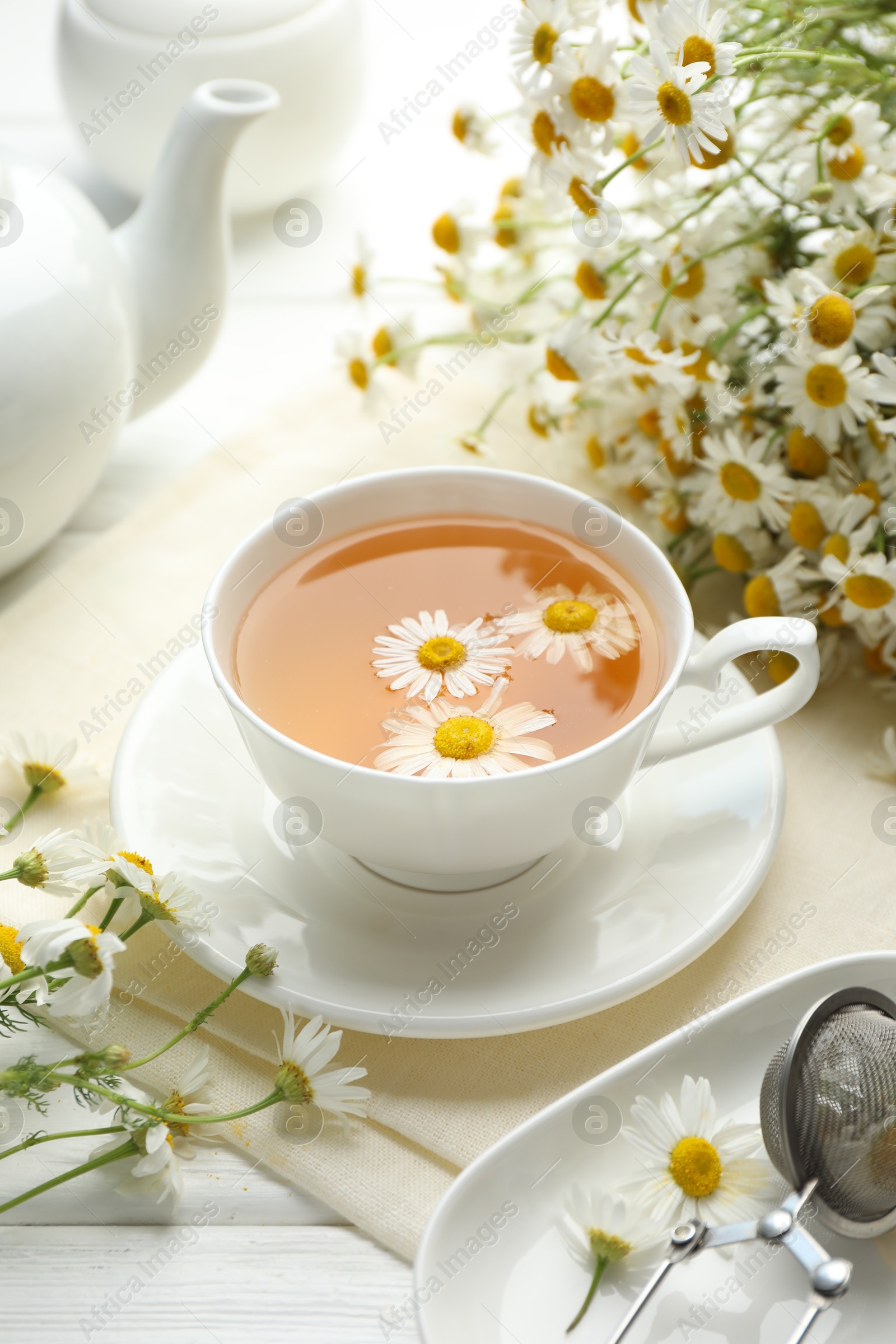 Tasty chamomile tea, infuser and flowers on white wooden table, closeup Photo of Tasty chamomile tea, infuser and flowers on white wooden table, closeup