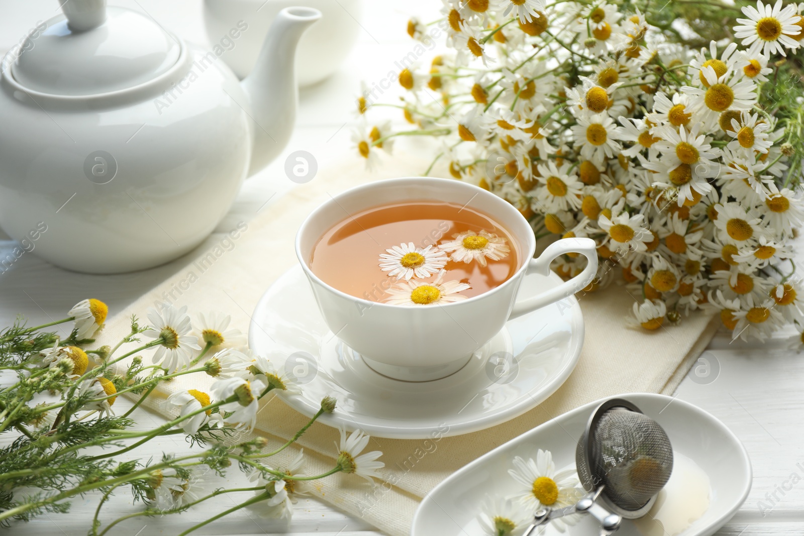 Tasty chamomile tea, infuser and flowers on white wooden table, closeup Photo of Tasty chamomile tea, infuser and flowers on white wooden table, closeup