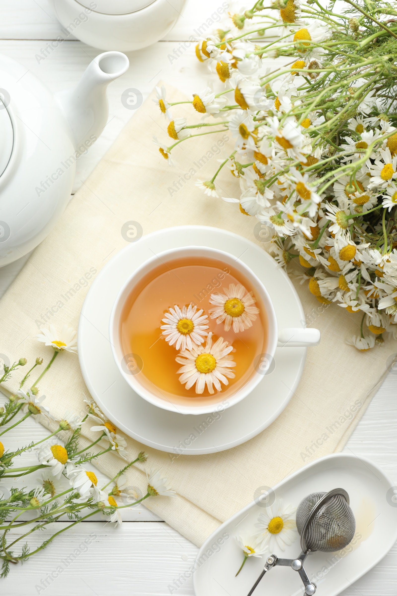Tasty chamomile tea, infuser and flowers on white wooden table, flat lay Photo of Tasty chamomile tea, infuser and flowers on white wooden table, flat lay
