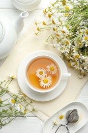 Photo of Tasty chamomile tea, infuser and flowers on white wooden table, flat lay