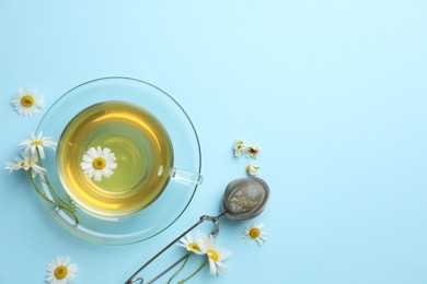 Photo of Tasty chamomile tea, infuser and flowers on light blue background, flat lay. Space for text