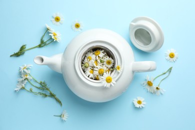 Photo of Teapot with chamomile flowers on light blue background, flat lay