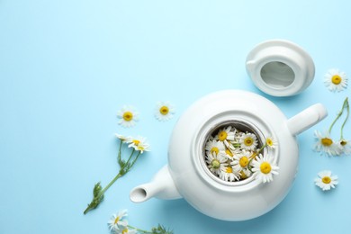 Photo of Teapot with chamomile flowers on light blue background, flat lay. Space for text