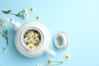 Photo of Teapot with chamomile flowers on light blue background, flat lay. Space for text