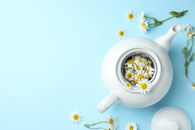Photo of Teapot with chamomile flowers on light blue background, flat lay. Space for text