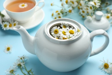 Photo of Teapot with chamomile flowers on light blue background, closeup