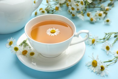 Photo of Tasty chamomile tea and flowers on light blue background, closeup