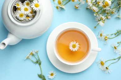 Photo of Tasty chamomile tea and flowers on light blue background, flat lay