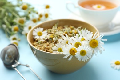 Photo of Chamomile flowers in bowl on light blue background, closeup